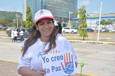 A young woman holds a sign in Spanish that reads “I create peace”