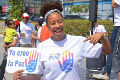 Una joven sostiene un cartel en español que dice “Yo creo la paz” 