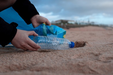 A person picking up a plastic bottle on a beach