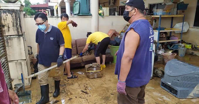 Un grupo de hombres de aspecto agotado trabaja entre objetos domésticos en un patio dañado por las inundaciones.