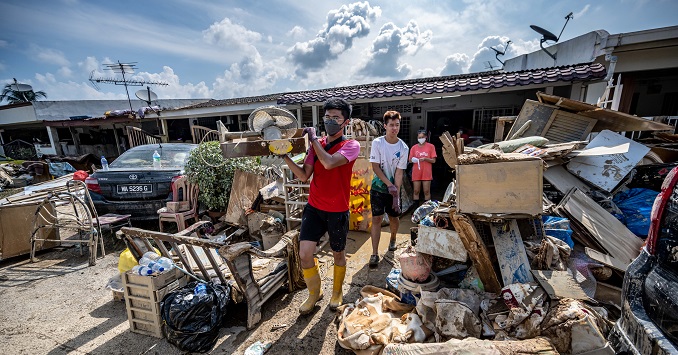 Furniture is piled up outside a house and two men carry goods onto the pile.