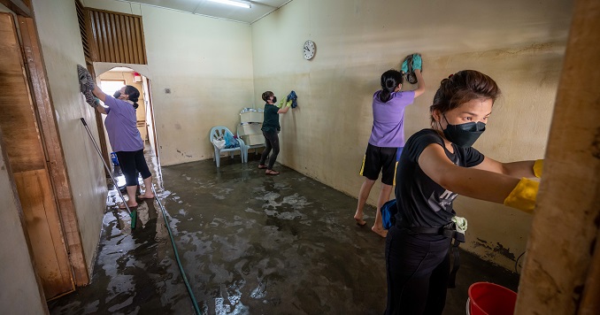 Four women wipe down the inner walls of a flood-damaged room.