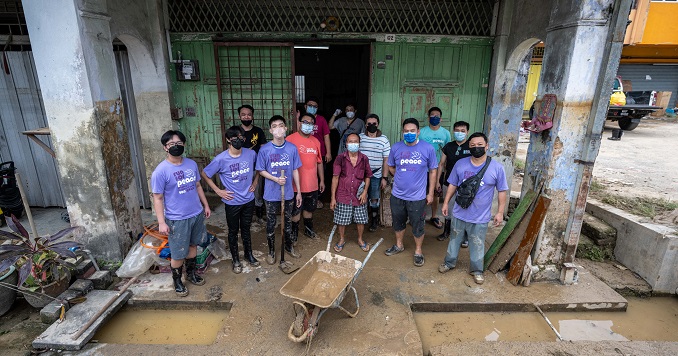 Una foto de grupo de una docena de hombres con una carretilla afuera de una casa dañada.