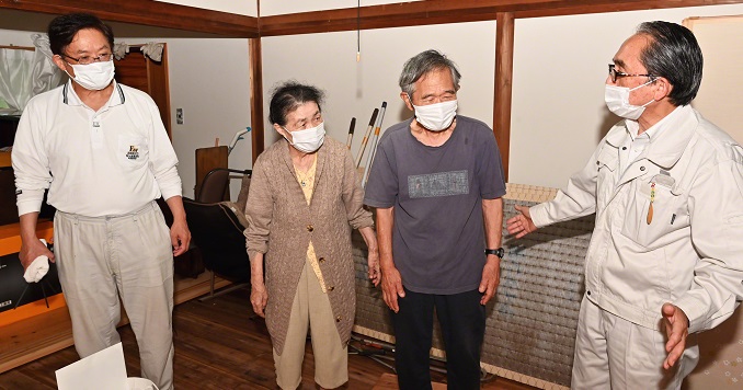 A group of three men and a woman standing and talking in a room