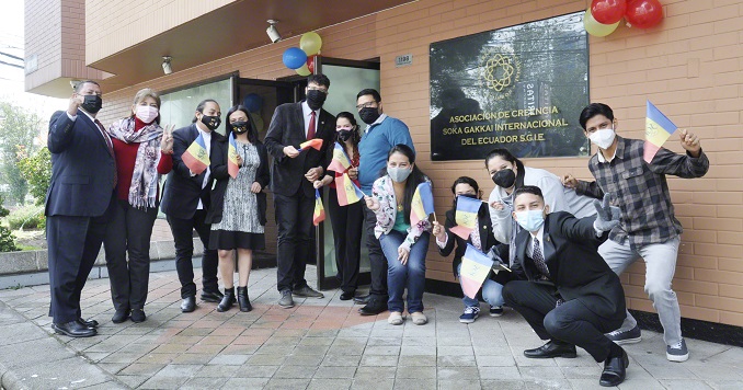 Un pequeño grupo de personas con banderas posan frente a un centro de la Soka Gakkai