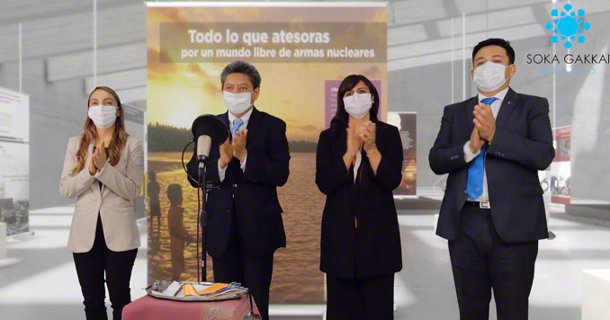 Two men and two women applaud at a podium in front of an exhibition panel