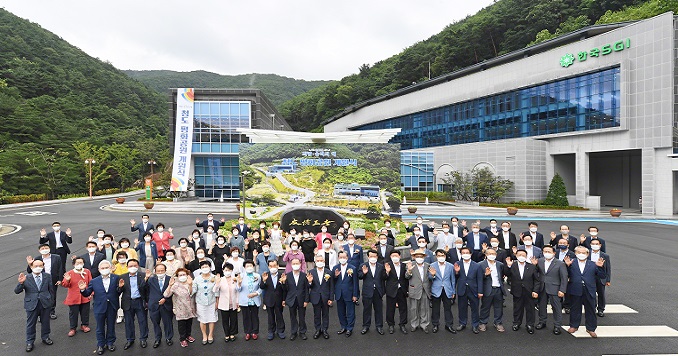 A large group of people pose for a commemorative photo outside a large building in hilly countryside