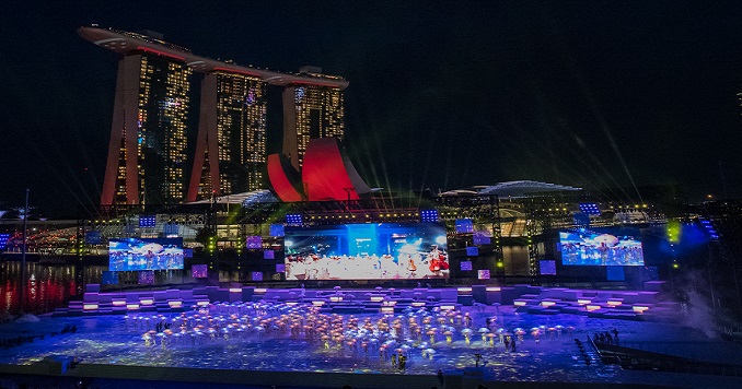 A large group of people performing group choreography at night in an outdoor space under stage lighting