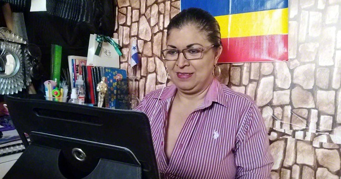 Una mujer sentada frente a su computadora con una bandera tricolor de la SGI en la pared detrás de ella.
