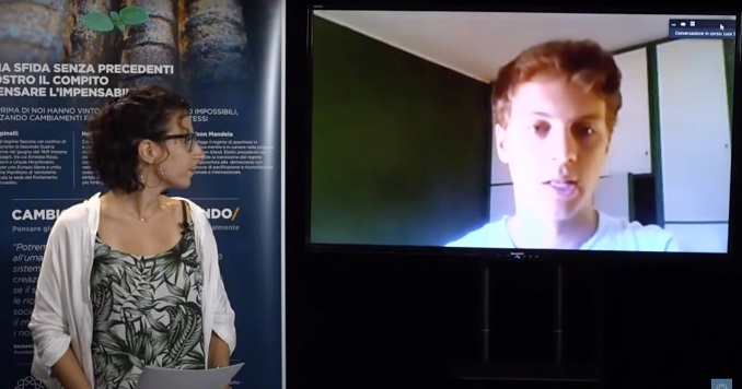 Una mujer que se encuentra frente a un panel de la exhibición mira hacia una pantalla en la que aparece un hombre hablando