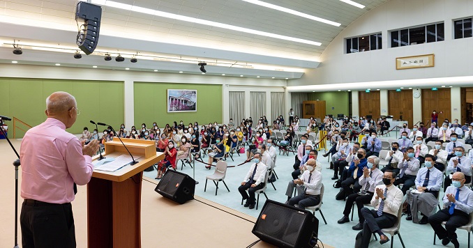 A man addresses a hall full of seated people from a podium