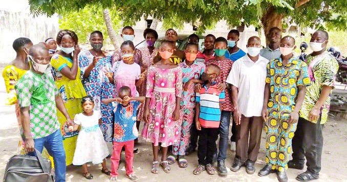 A group of around 20 men, women and children in masks pose for a photo outdoors