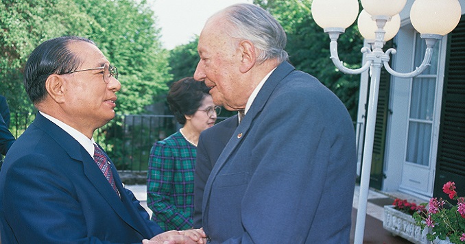 Ikeda y Huyghe, de pie frente a frente, estrechándose las manos, frente a un edificio