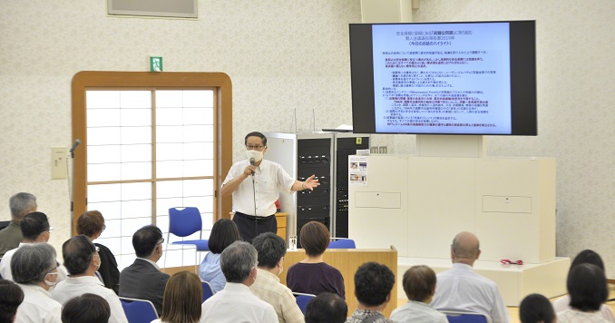 A man speaks in front of a seated audience in a hall