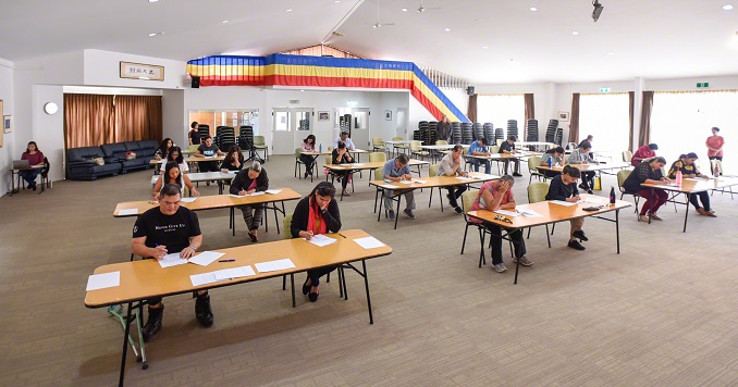 Exam participants take the exam at tables in a small hall