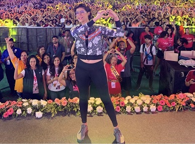 Tahira stands before a large crowd, everyone making heart signs with their hands