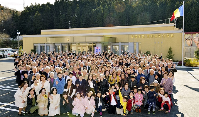 A group photo of around 200 smiling people outside a Soka Gakkai center.