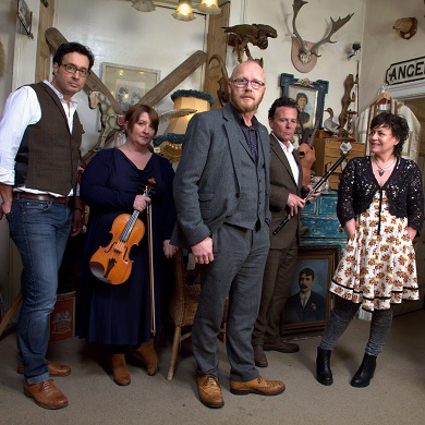 Three men and two women, some holding musical instruments, facing the camera