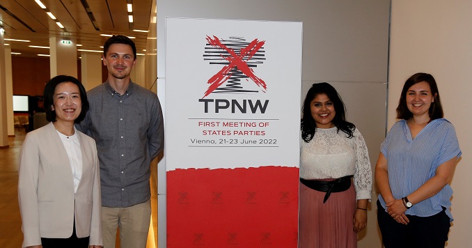 Dos jóvenes de pie a cada lado de un cartel que dice “TPNW” (TPAN) 