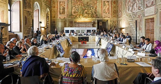 People seated around a table in a room with historical paintings adorning the walls.